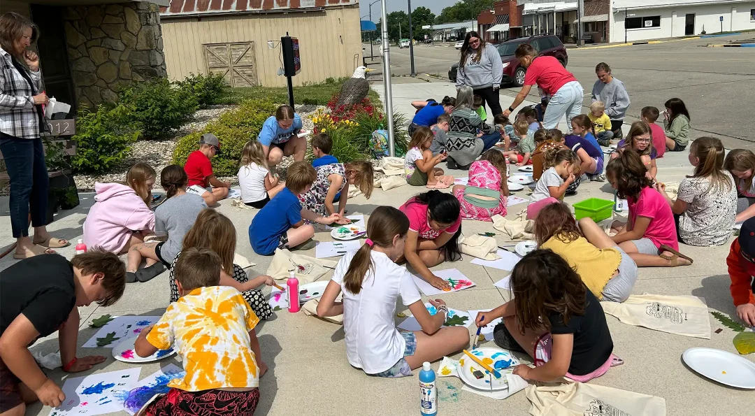 A group of children coloring and painting their reading bags outside from a local library event.