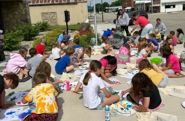 A group of children coloring and painting their reading bags outside from a local library event.