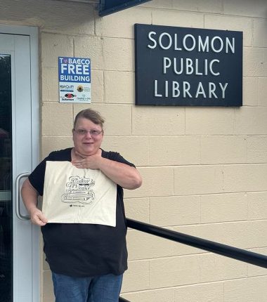A librarian receives a bunch of “Color Our World” reading bags at the Solomon Public Library as part of the summer reading program.