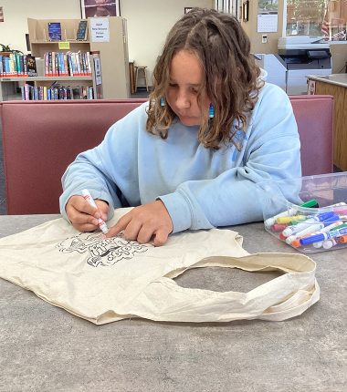 A young girl inside the Minneapolis Public Library coloring her “Color Our World” reading bag from Twin Valley.