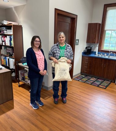 Two women at the Public Library holding up their “Color Our World” reading bags.